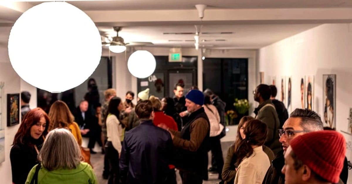 Guests mingling at an evening reception in a white-walled Bernal Heights art gallery under round globe lights