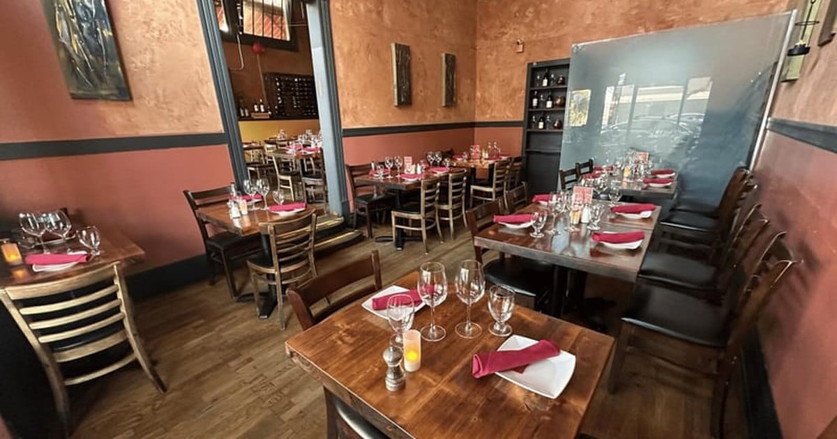 Private dining room in San Francisco with terracotta walls, wooden tables set with wine glasses and red napkins, and paintings on the walls