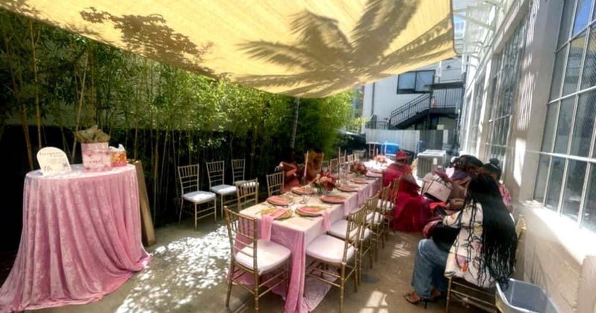 Guests at long tables with pink linens on a shaded outdoor patio beside a San Mateo art studio