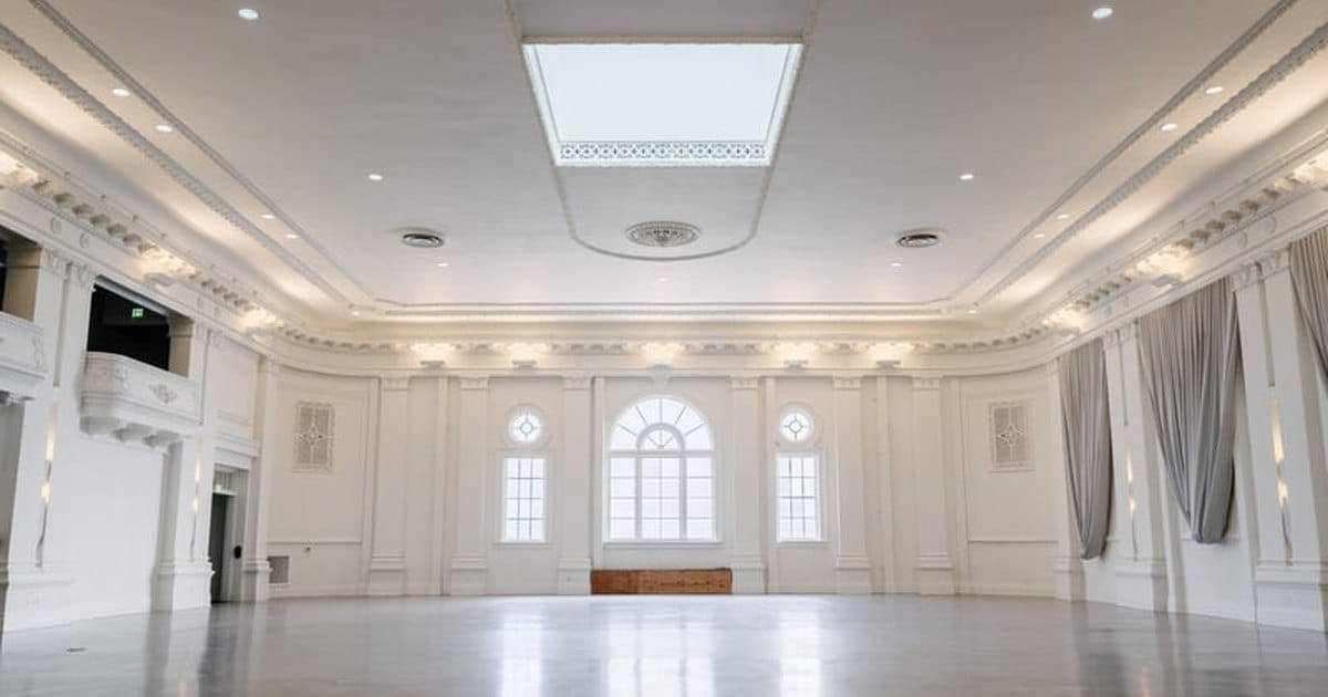 Empty white ballroom in San Francisco with arched windows, a skylight and a polished floor