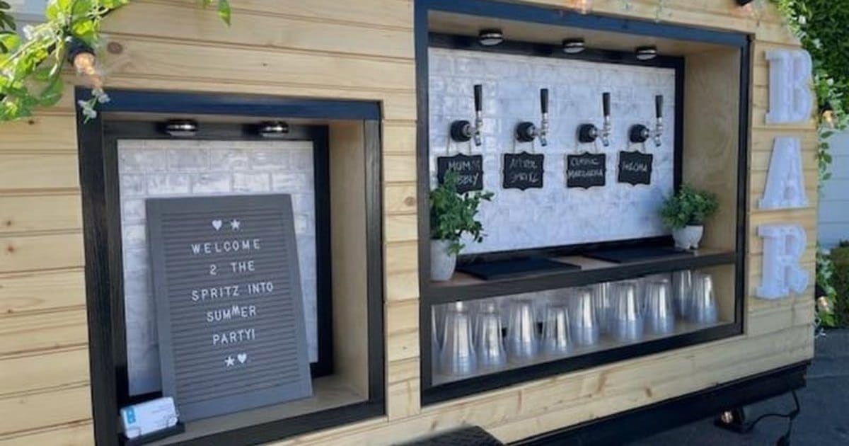 Wooden tap trailer from a Santa Rosa mobile bar service, with four taps, chalkboard drink labels, a letter board welcome sign and greenery with string lights along the roof