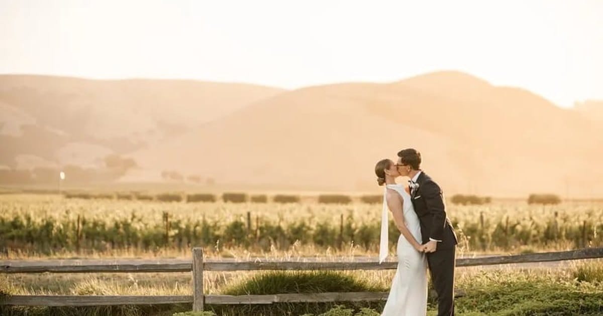 Bride and groom kissing beside a wooden fence at the edge of a vineyard in warm evening light, a still from a Napa wedding videographer's package