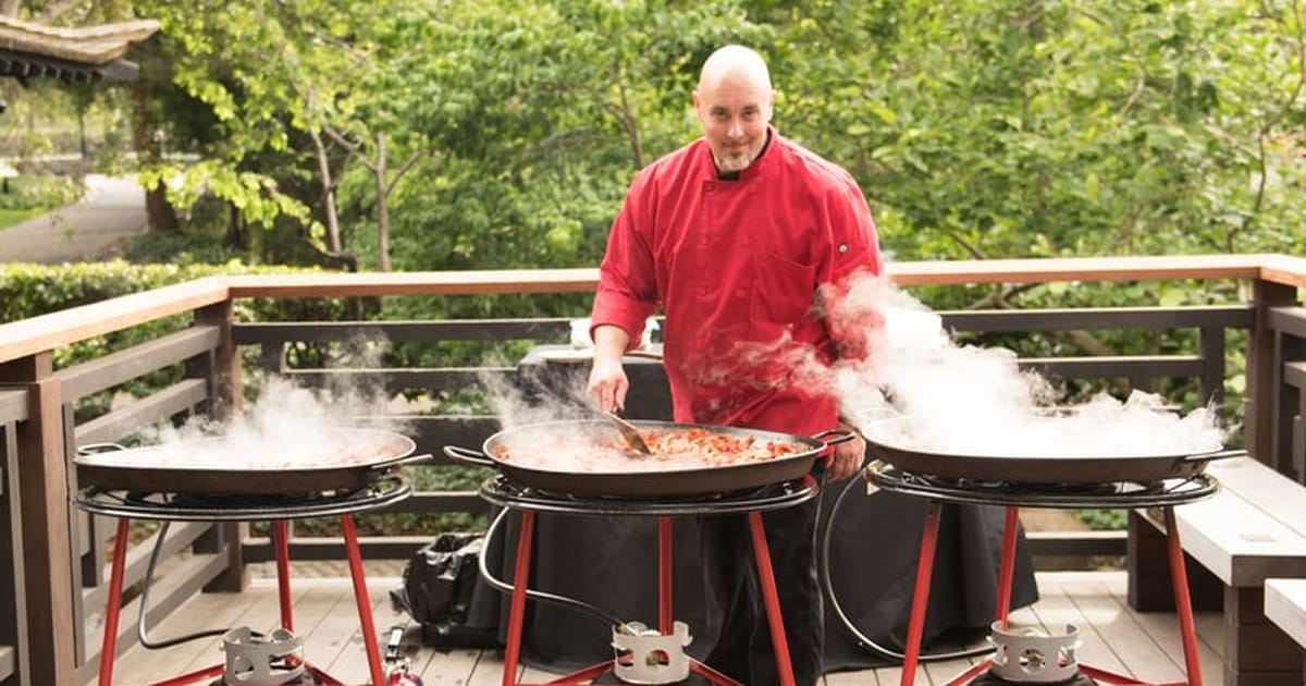 Chef cooking paella in three large traditional pans on an outdoor deck, from a San Francisco caterer