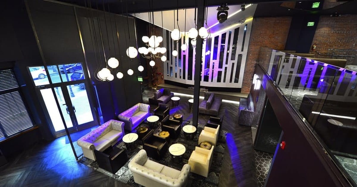 Overhead view of a dark San Francisco event lounge with globe pendant lights, white tufted sofas and purple uplighting