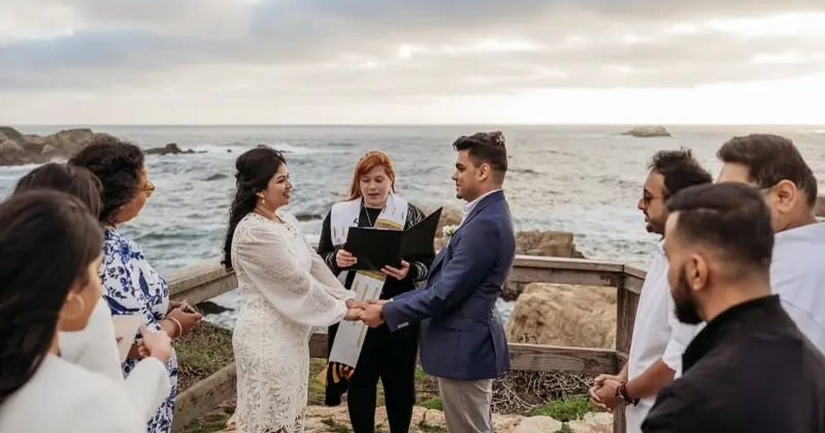Monterey wedding officiant in a black robe leading a small cliffside ceremony above the ocean, with guests standing on both sides