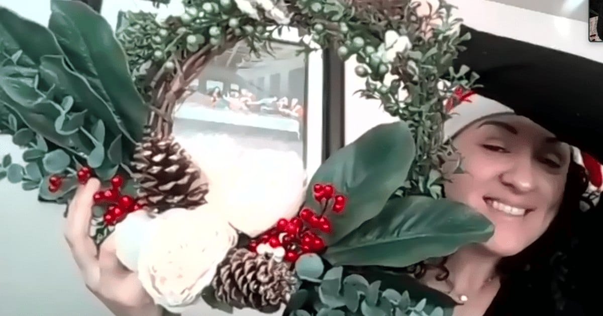 Smiling woman on a video call holding up her finished holiday wreath from a virtual wreath making class