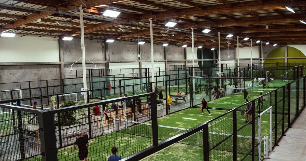Indoor padel courts under a warehouse roof in South San Francisco, seen from a raised walkway
