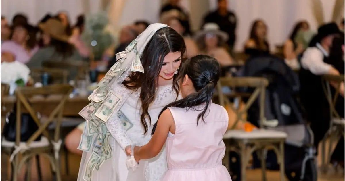 Bride with paper money pinned to her veil dancing with a young girl in a pink dress at a wedding reception