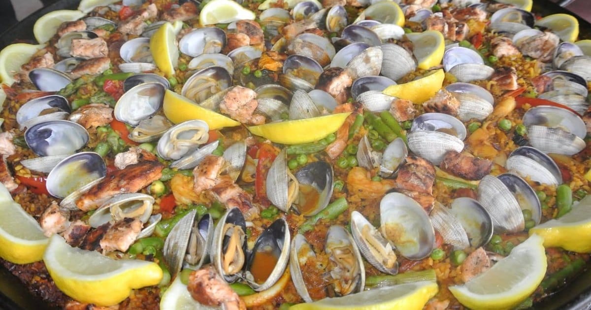 Large pan of paella with clams, shrimp, chicken, peas and lemon wedges from a San Francisco caterer