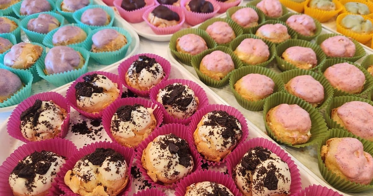 Trays of mini cream puffs in pink, green, teal and yellow paper liners, topped with cookie crumbs, pink, purple and green glazes and chocolate