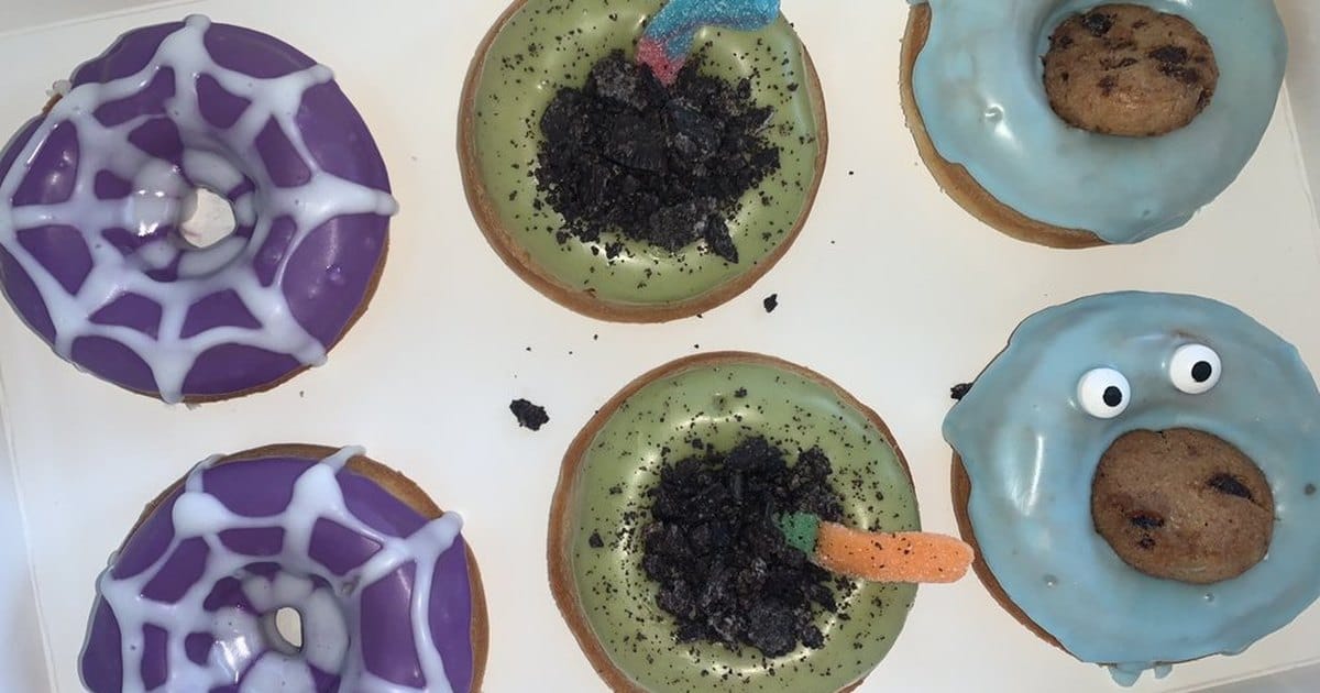 Halloween-decorated mochi donuts with spider-web glaze, cookie-crumb toppings and candy eyes in a white box from a Hercules bakery