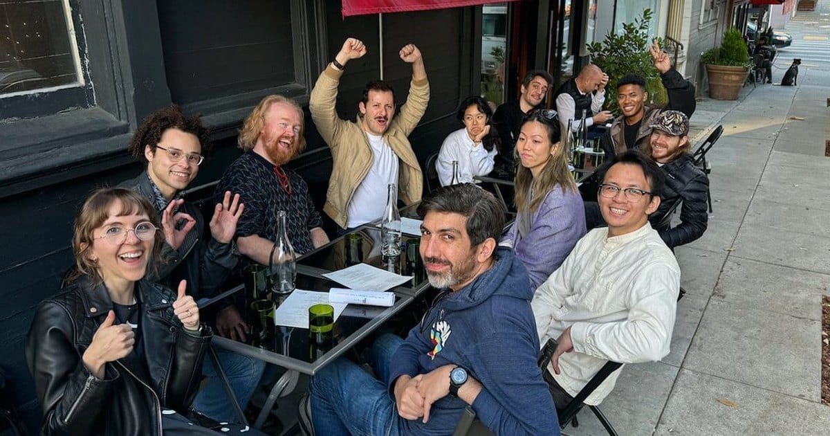 Scavenger hunt team cheering with raised arms at outdoor cafe tables under a red awning