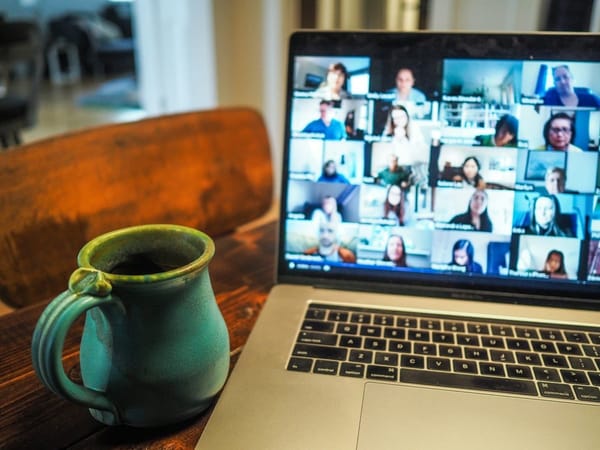 Laptop on a wooden table showing a video call grid of remote team members, next to a coffee mug