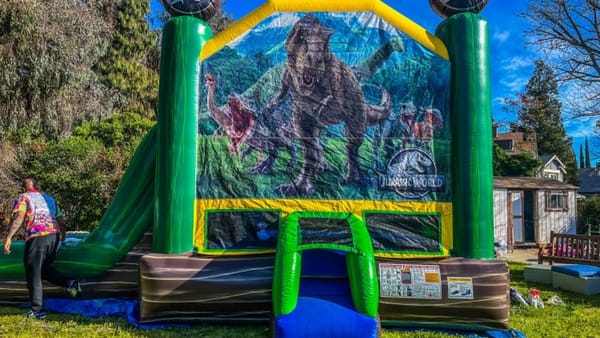 Jurassic World themed bounce house combo with slide set up on a backyard lawn for an East Bay party