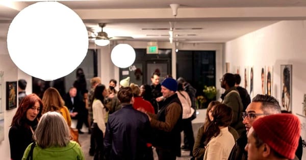 Guests mingling at an evening reception in a white-walled Bernal Heights art gallery under round globe lights