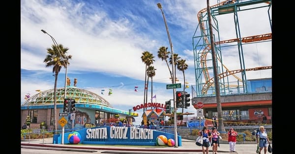 Entrance to the Santa Cruz Beach Boardwalk with a Santa Cruz Beach sign, palm trees and a roller coaster