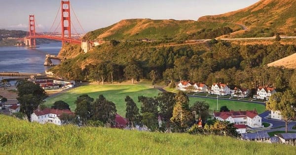 Cavallo Point in Sausalito: white red-roofed buildings around a green lawn below grassy hills, with the Golden Gate Bridge behind