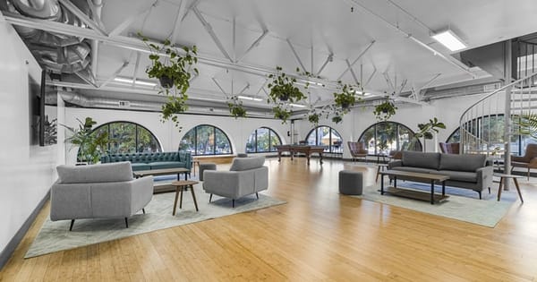 Team offsite venue in Redwood City: open loft with gray sofas and armchairs, hanging plants, light wood floors and arched windows