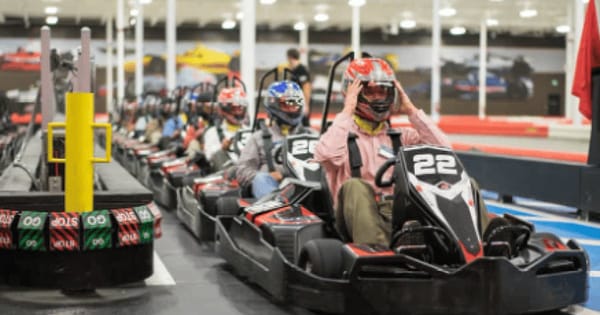 Drivers in helmets lined up in electric go-karts on an indoor track in Santa Clara