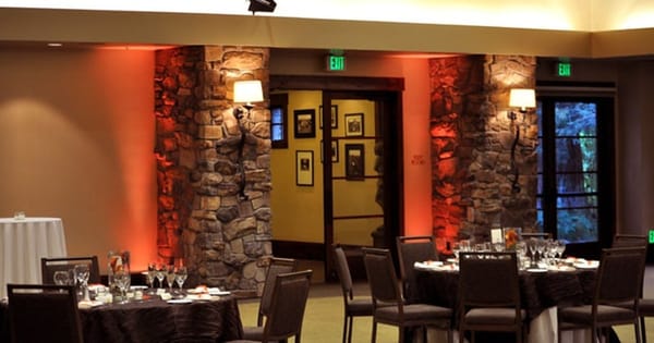 Dining room set with round tables and dark linens, with amber uplights washing two stone columns