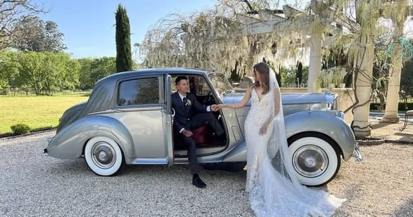 Bride and groom at the open rear door of a two-tone silver 1954 Bentley wedding car on a gravel drive