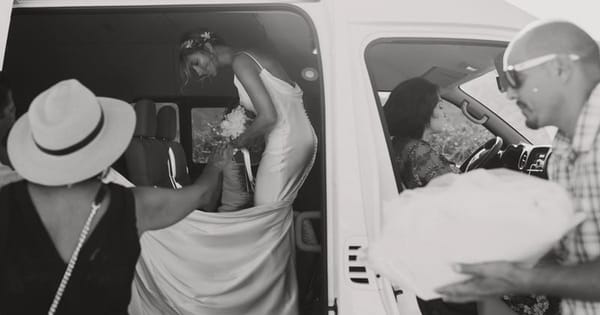 Black and white photo of a bride in a white gown stepping out of a van while guests help with her dress, from a San Francisco wedding content creator package