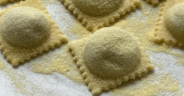 Rows of handmade square ravioli dusted with semolina on a white work surface