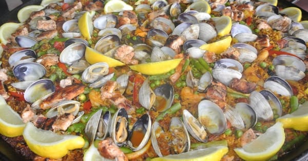Large pan of paella with clams, shrimp, chicken, peas and lemon wedges from a San Francisco caterer
