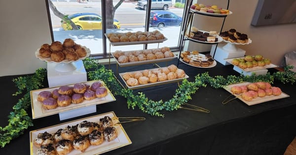 Catered dessert table by a window with trays and tiered stands of cream puffs and mini pastries along a green garland