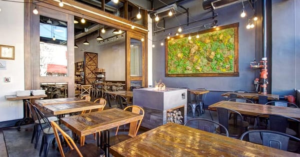 Restaurant dining room with wooden tables, metal chairs, a gas fire table, string lights and a framed moss wall panel