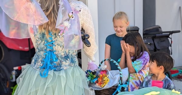 Costumed fairy entertainer from a Fremont body art listing, seen from behind at a party table as smiling kids gather around