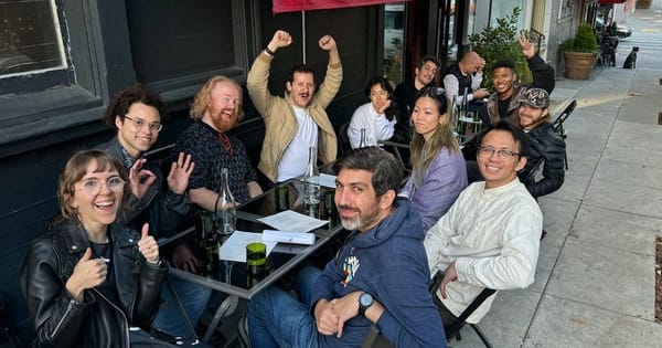 Scavenger hunt team cheering with raised arms at outdoor cafe tables under a red awning